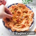 Hand dipping pita chip in sundried tomato feta dip on a small blue and white plate.
