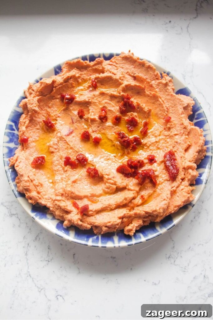 Instant Sun-Kissed Feta Dip 8 Chopped sundried tomatoes on top of sundried tomato feta dip smoothed out onto a small blue and white plate, ready to serve.
