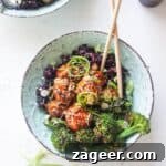 Glazed Asian chicken meatballs with rice and broccoli in a small blue bowl, garnished with sesame seeds and scallions.
