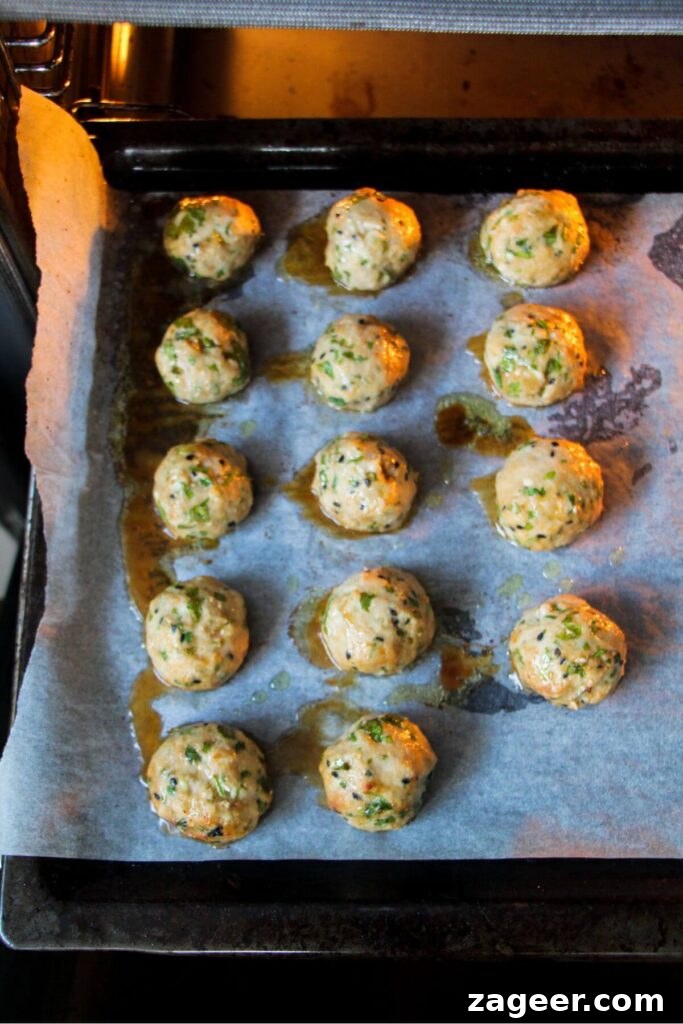 Sticky Gochujang Chicken Meatballs 6 Par-cooked chicken meatballs on a lined oven tray, partially baked.