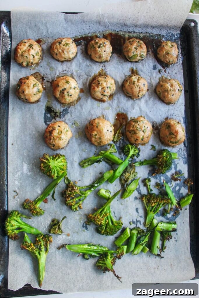 Sticky Gochujang Chicken Meatballs 7 Cooked chicken meatballs and beautifully charred broccolini on a lined oven tray, freshly out of the oven.