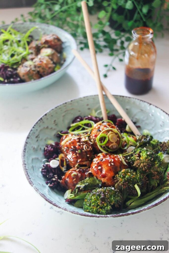 Sticky Gochujang Chicken Meatballs 8 Glazed Asian chicken meatballs with rice and broccoli in a small blue bowl, showcasing the final dish.