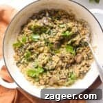 Mushroom orzo in a large white skillet with a large silver spoon.
