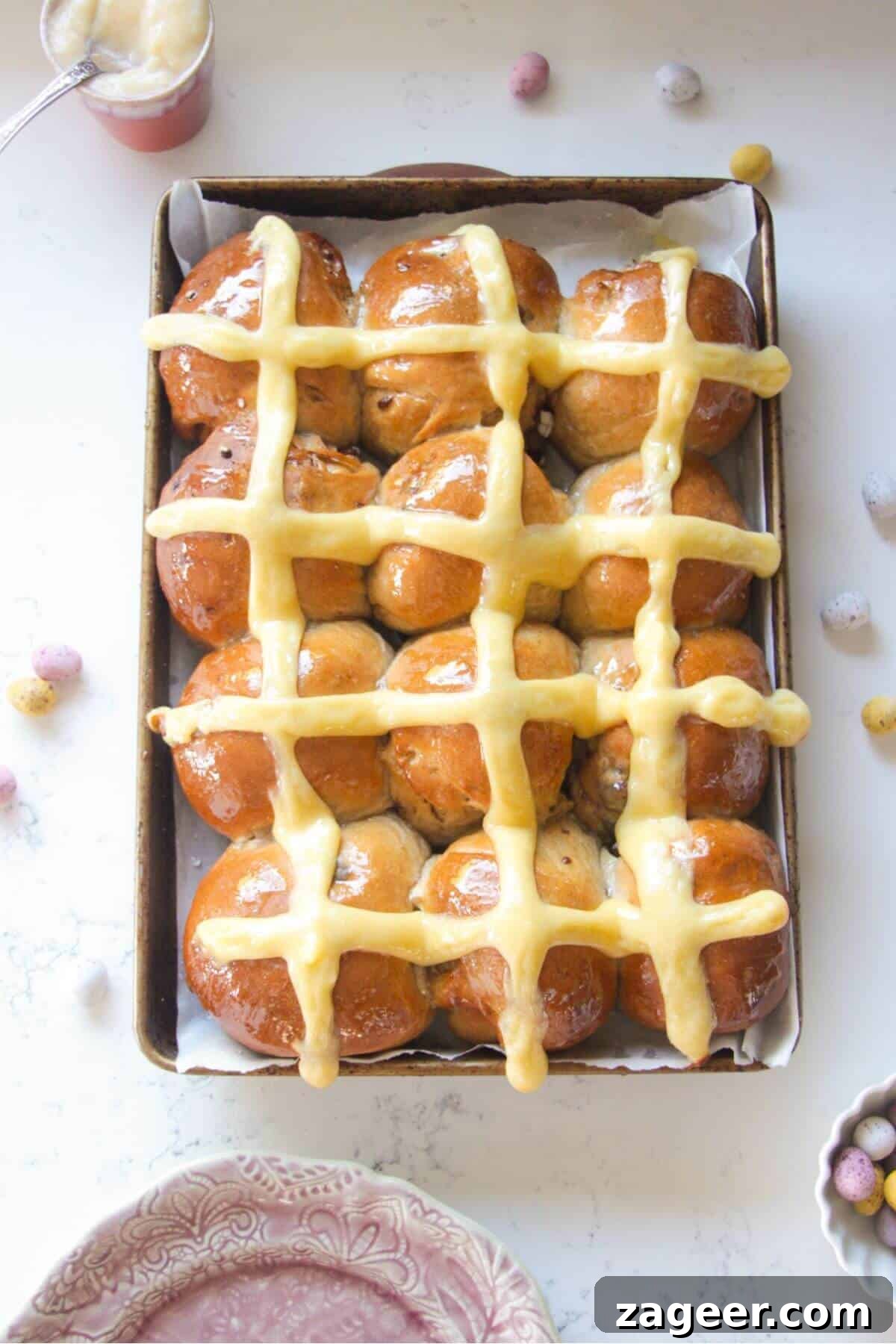 Easter Mini Egg Chocolate Hot Cross Buns 2 12 glazed mini egg chocolate hot cross buns in a lined oven tray with mini eggs on the bench next to them.