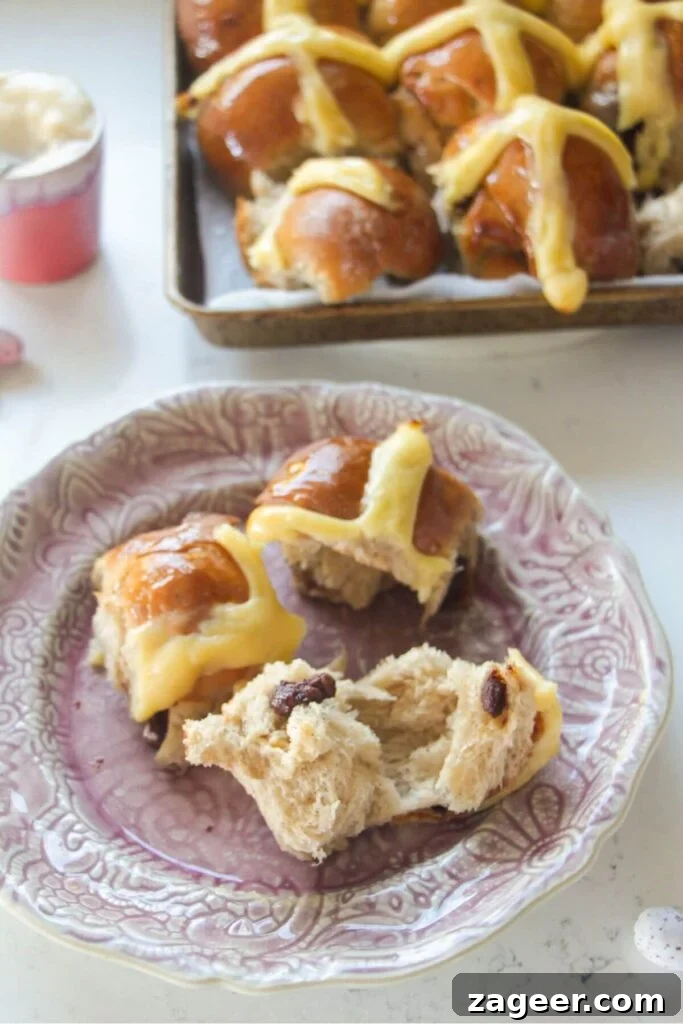 Easter Mini Egg Chocolate Hot Cross Buns 17 Torn open mini egg hot cross bun on a pink plate with more hot cross buns in the background.