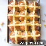 12 mini egg chocolate hot cross buns in a lined oven tray with more mini eggs on the side.