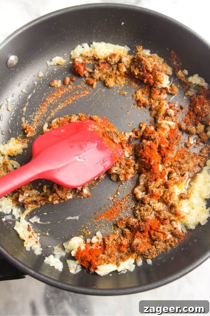 Speedy Chicken Rogan Josh 4 Finely diced onions sautéing in butter with a red spatula in a frying pan, ready for the addition of fragrant spices.