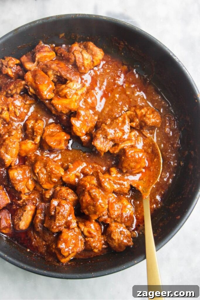 Speedy Chicken Rogan Josh 8 A close-up of the finished Chicken Rogan Josh, showcasing its thick, glossy gravy with a gold spoon resting inside.