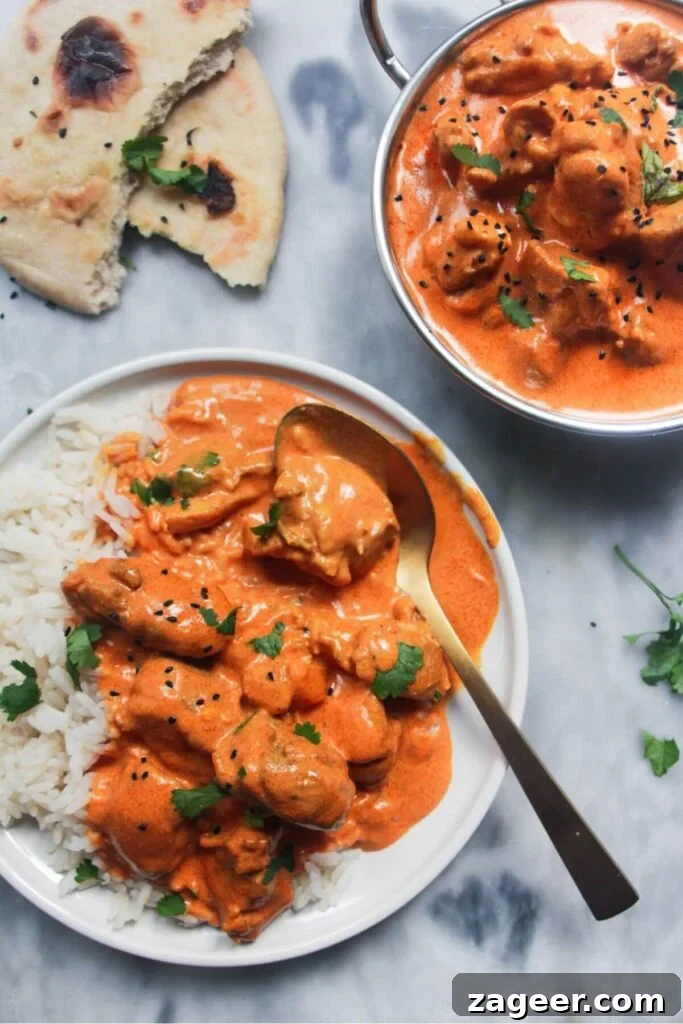 Speedy Chicken Rogan Josh 10 A white plate featuring rich butter chicken served alongside fluffy rice and warm garlic naan bread, a classic Indian meal.