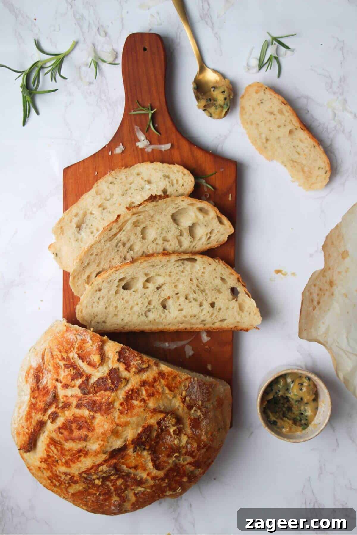 Artisan Style Rosemary Parmesan Bread Done Easy 2 3 slices of golden rosemary parmesan bread on a small wooden board with the rest of the loaf and garlic butter in the background.