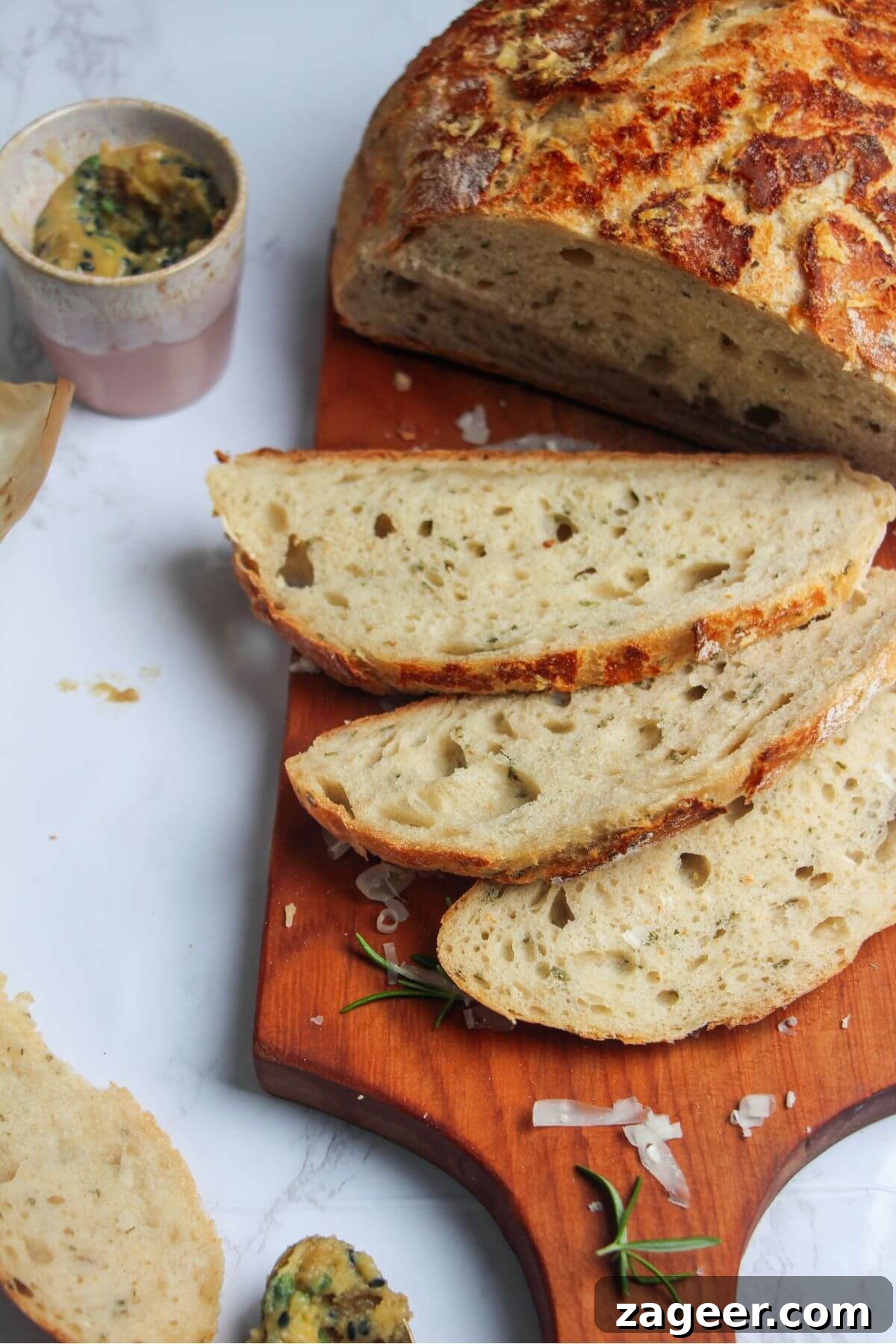 Artisan Style Rosemary Parmesan Bread Done Easy 16 3 slices of bread on a small wooden board with the rest of the load behind.