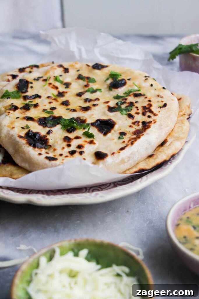 Effortless Two Ingredient Cheesy Naan 11 A close-up view of several cheese stuffed naans piled high on a white plate, with a bowl of grated cheese in the foreground.