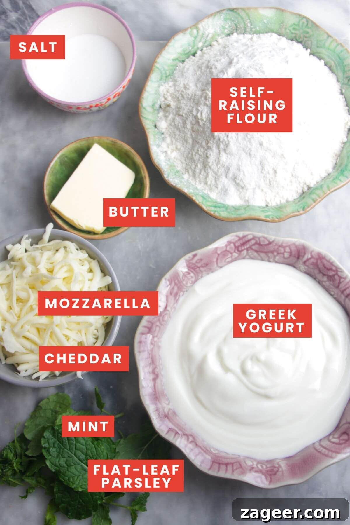 Effortless Two Ingredient Cheesy Naan 3 Ingredients for cheese naan, including self-raising flour, Greek yogurt, various cheeses, and fresh herbs, neatly arranged on a grey marble background.