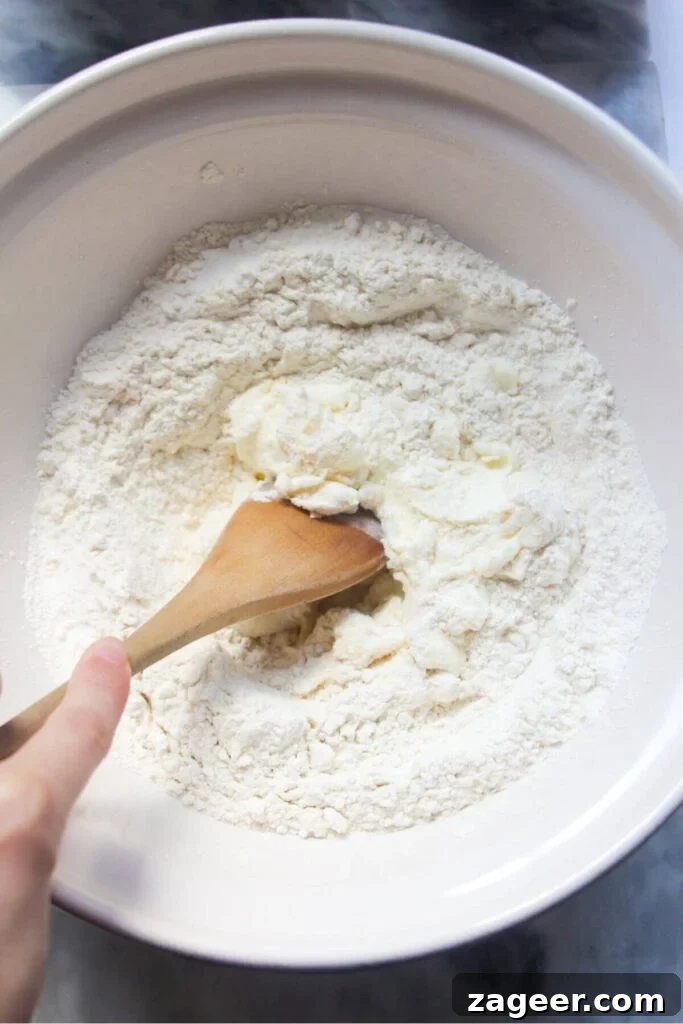 Effortless Two Ingredient Cheesy Naan 4 Flour and Greek yogurt in a large white ceramic bowl, ready to be mixed with a wooden spoon to form the dough.