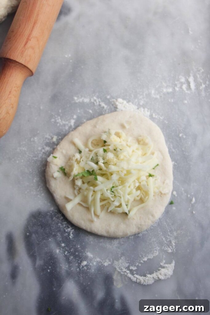 Effortless Two Ingredient Cheesy Naan 7 A generous pile of cheese and herbs placed onto a small circle of naan dough, ready to be folded and sealed.