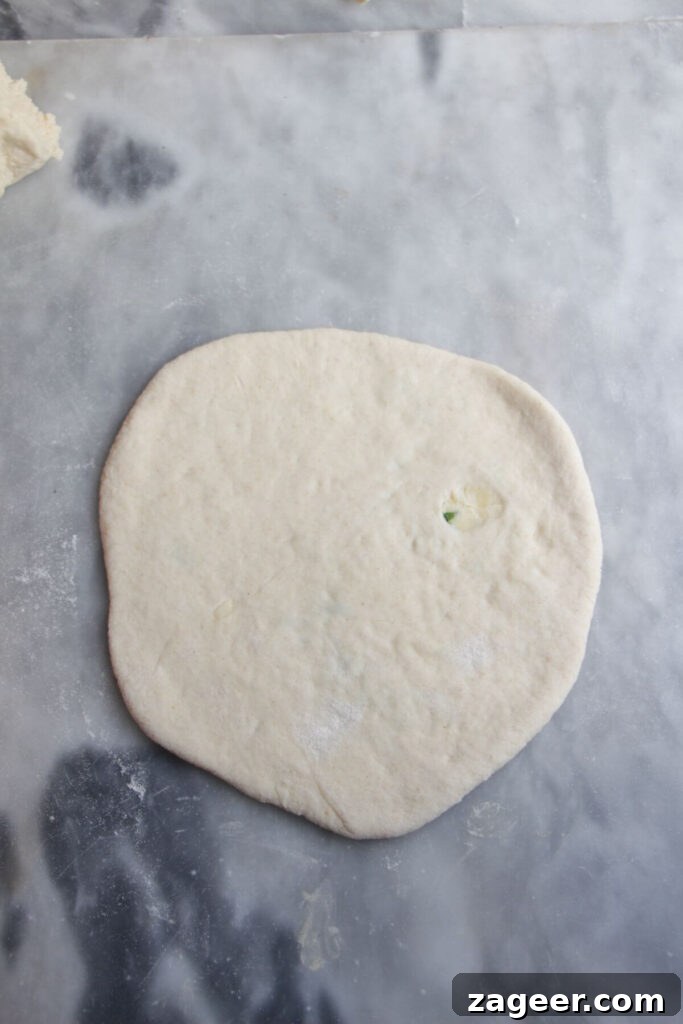 Effortless Two Ingredient Cheesy Naan 9 A perfectly rolled out cheese stuffed naan resting on a grey marble background, ready for cooking.