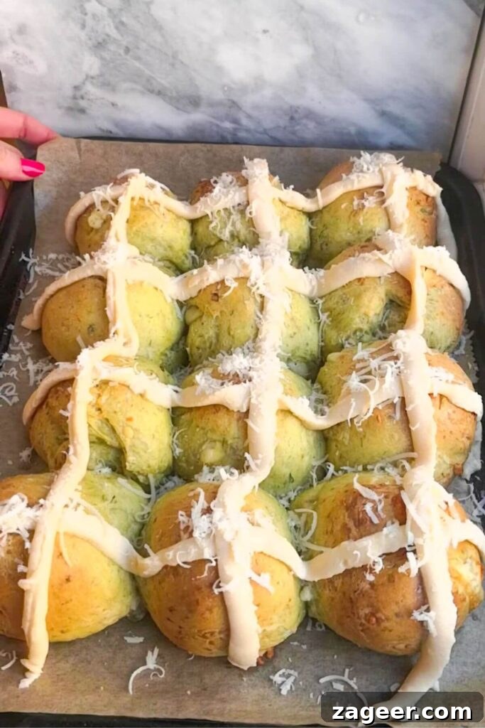 Wild Garlic & Cheddar Savory Hot Cross Buns 12 Twelve wild garlic hot cross buns, each adorned with creamy béchamel sauce crosses, are arranged on an oven tray, freshly piped and ready for their final bake.