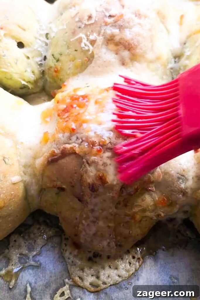 Wild Garlic & Cheddar Savory Hot Cross Buns 13 A small red brush applies a glossy layer of sweet chilli jam glaze to a baked wild garlic bun on a baking tray.