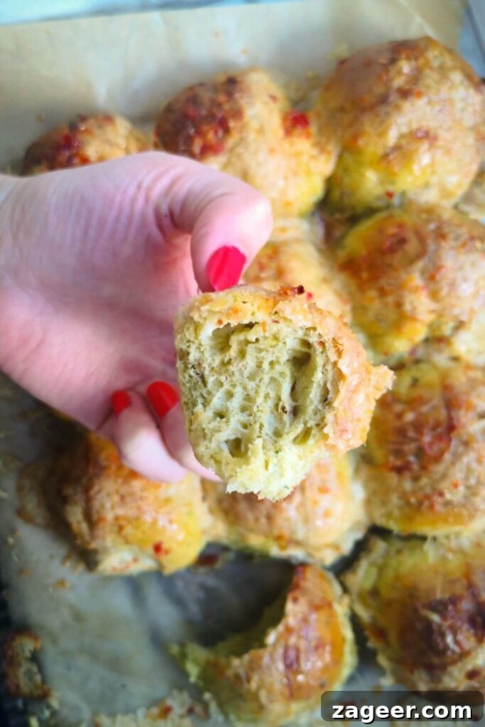 Wild Garlic & Cheddar Savory Hot Cross Buns 14 Close up of a hand holding a piece of a freshly baked wild garlic hot cross bun, revealing its soft interior and melted cheese.