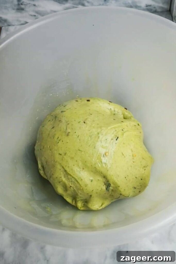 Wild Garlic & Cheddar Savory Hot Cross Buns 4 The smooth and elastic wild garlic hot cross bun dough, beautifully risen and puffy, rests in a large clear bowl, ready for the next stage of baking.