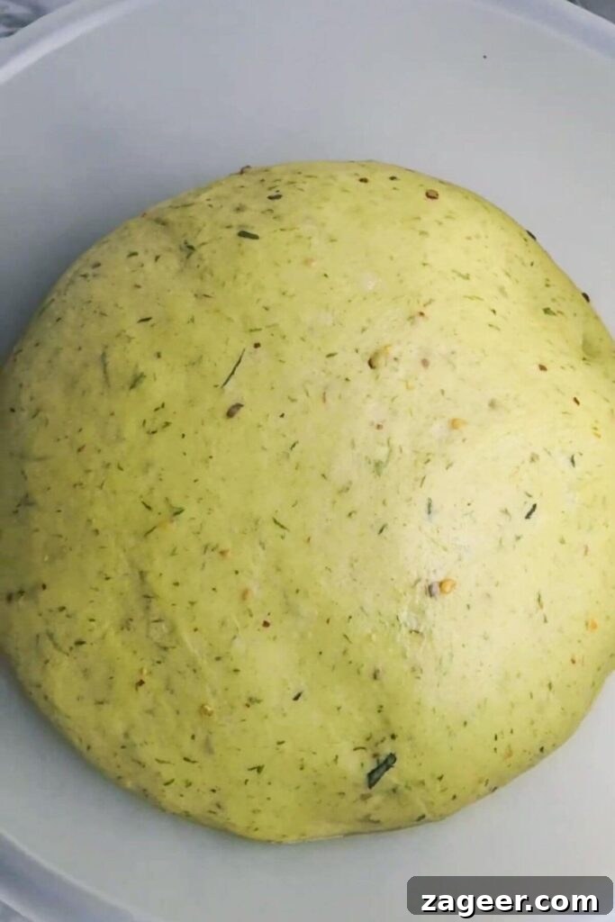 Wild Garlic & Cheddar Savory Hot Cross Buns 5 The airy, expanded wild garlic hot cross bun dough fills a clear mixing bowl, indicating a successful first rise.