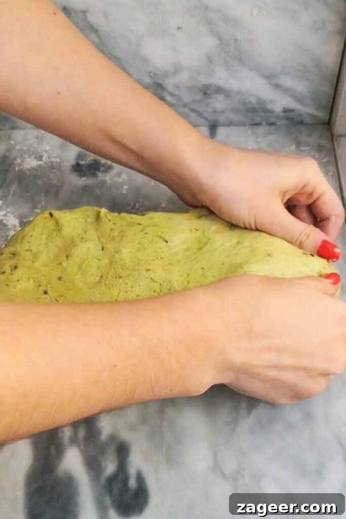 Wild Garlic & Cheddar Savory Hot Cross Buns 7 Close-up view of hands meticulously sealing the edges of the cheese-filled dough, creating a neat parcel.