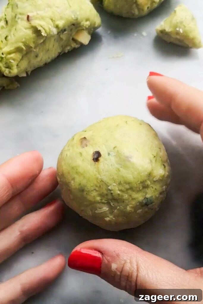 Wild Garlic & Cheddar Savory Hot Cross Buns 9 Hands meticulously form a smaller ball from a portion of the wild garlic hot cross bun dough, demonstrating the individual shaping process.