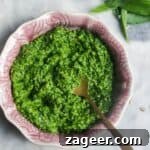 Bright green wild garlic pesto in a small pink bowl on a grey marble background.