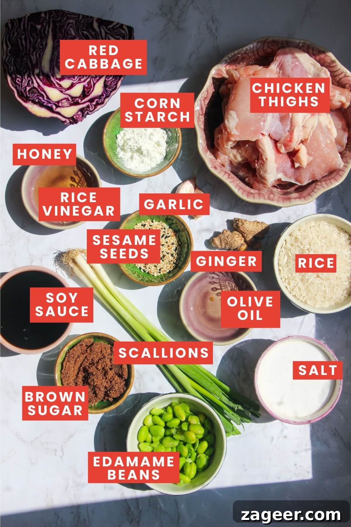 Hearty Teriyaki Chicken Rice Bowls 3 Ingredients for chicken teriyaki bowls laid out on a white marble background including chicken, soy sauce, honey, brown sugar, garlic, ginger, rice, and various fresh vegetables.