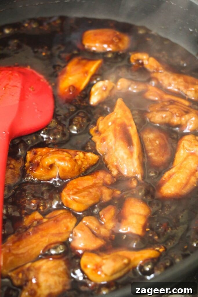 Hearty Teriyaki Chicken Rice Bowls 6 Teriyaki sauce being tossed through chicken in a large frying pan, creating a glossy coating.