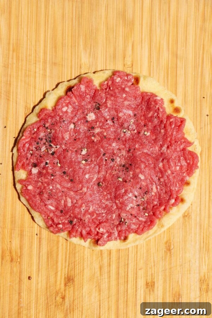 Big Mac Smash Burger Taco Fusion 5 A golf-ball sized portion of raw ground beef is meticulously pressed into a thin, even layer across a small flour tortilla, ready for cooking.