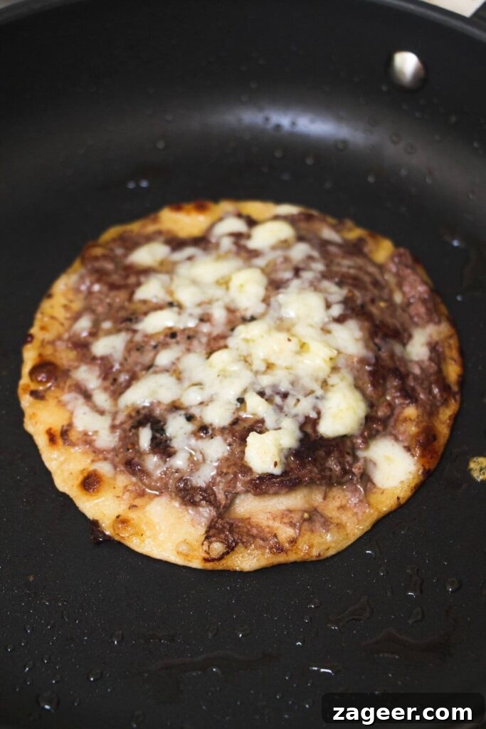 Big Mac Smash Burger Taco Fusion 7 Melted grated cheese generously covering the cooked ground beef on a small flour tortilla, sizzling gently in a frying pan, indicating it's almost ready.