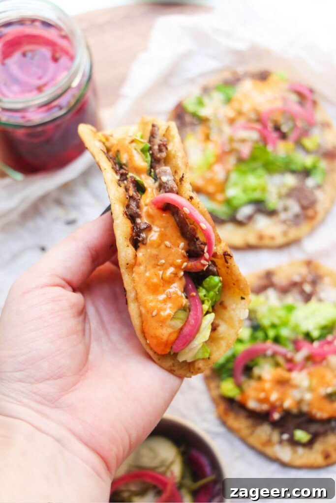 Big Mac Smash Burger Taco Fusion 9 A hand proudly holds up a freshly made Big Mac taco, showcasing its delicious layers, with more finished tacos blurred in the background, ready to be devoured.