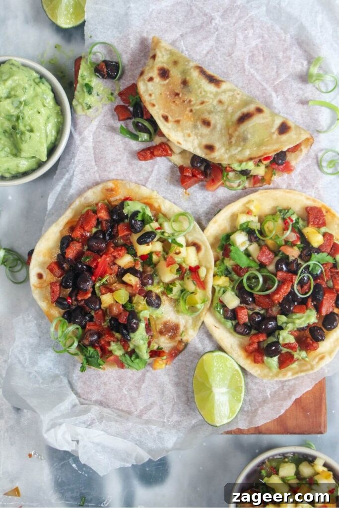 Spicy Chorizo and Black Bean Tacos with Sweet Pineapple Salsa 8 A close-up of three colourful chorizo black bean tacos, beautifully arranged on a baking paper-lined wooden board, with side dishes of whipped avocado and pineapple salsa.