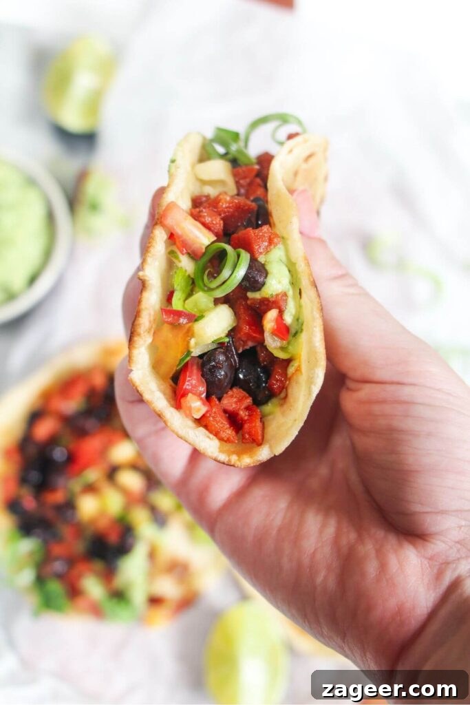 Spicy Chorizo and Black Bean Tacos with Sweet Pineapple Salsa 9 A hand holding up a freshly assembled chorizo and black bean taco, showcasing its vibrant fillings, with more tacos visible in the softly blurred background.