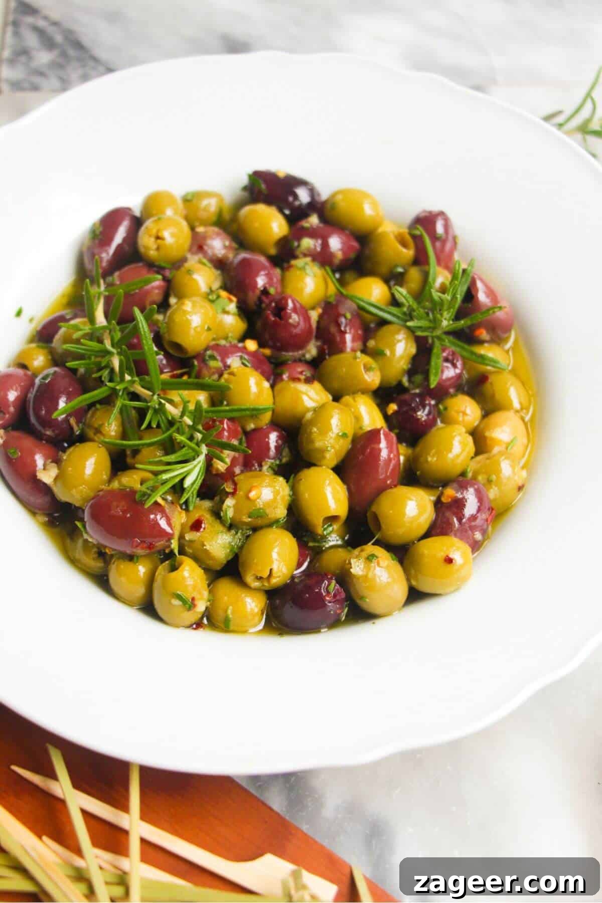 Zesty Olives in Minutes 2 Close up of a white scalloped bowl of marinated olives, with skewers on the side, ready to be served.