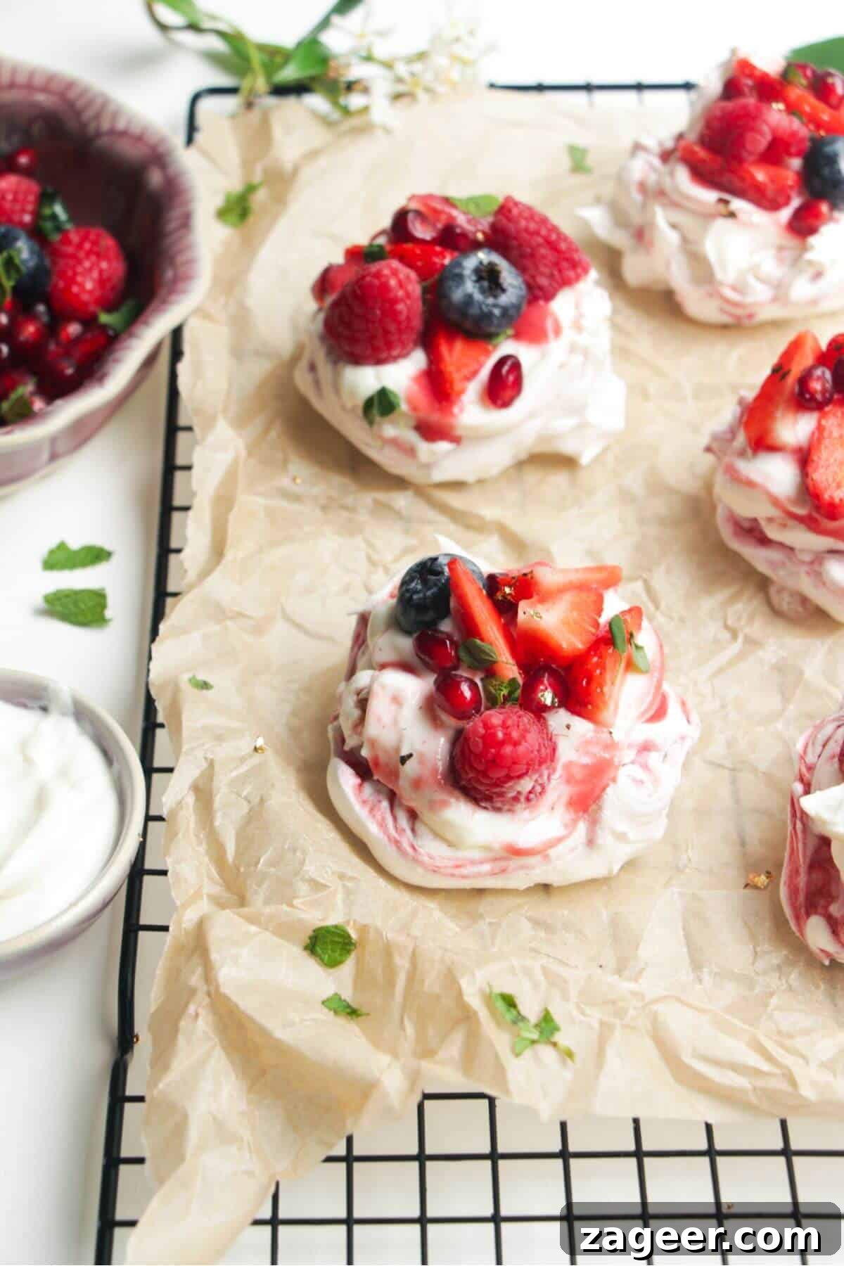Heavenly Berry Ripple Cheesecake Pavlova Bites 2 Two mini, berry topped pavlovas on a baking paper lined wire rack with more pavlovas behind them.