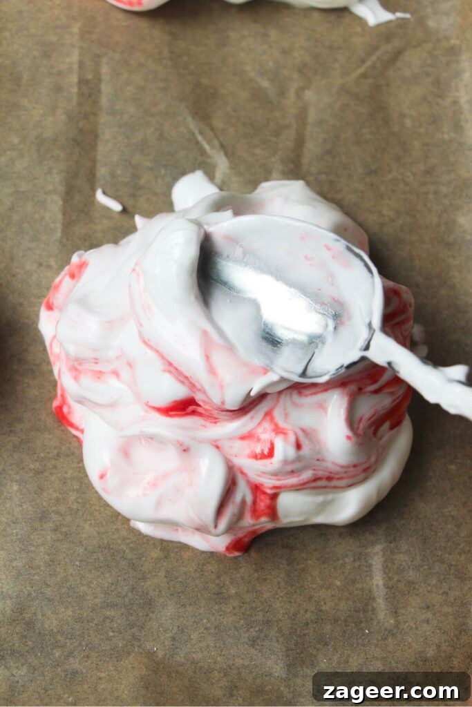 Heavenly Berry Ripple Cheesecake Pavlova Bites 11 Silver spoon creating crater in the top of a mini pavlova.