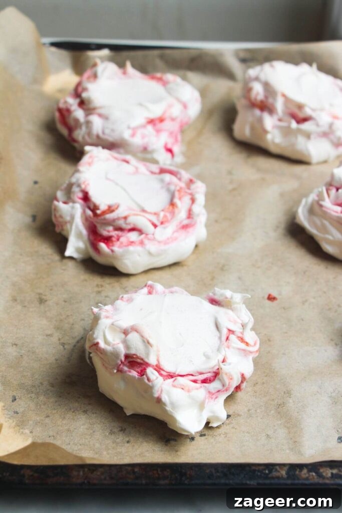 Heavenly Berry Ripple Cheesecake Pavlova Bites 13 Close up of berry ripple pavlovas on a lined baking tray.