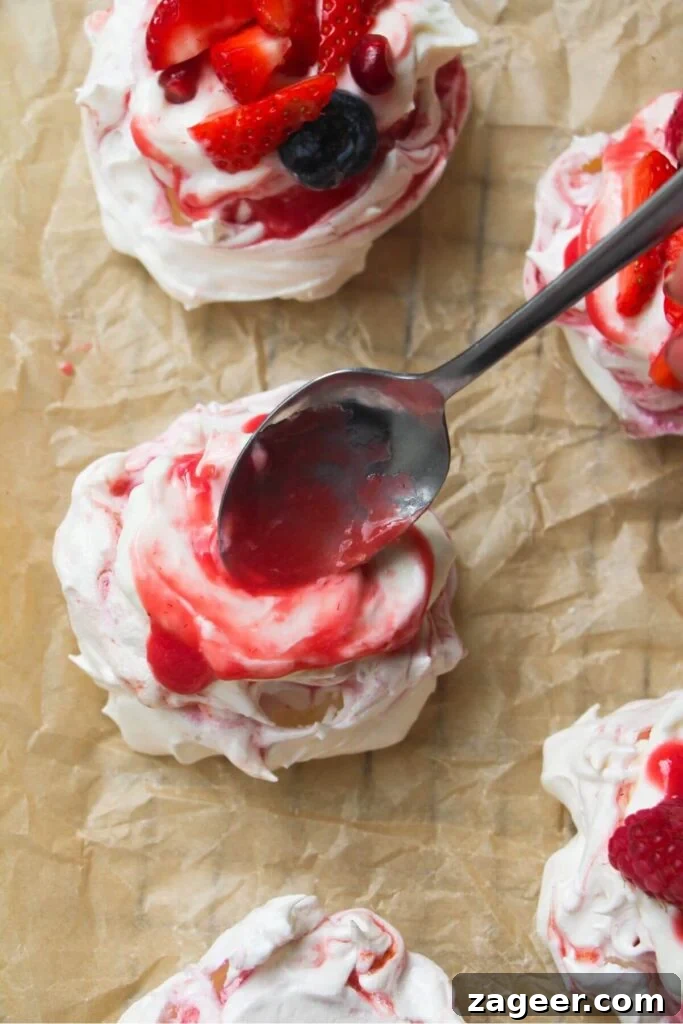 Heavenly Berry Ripple Cheesecake Pavlova Bites 16 Spooning berry puree onto mini pavlova on a lined baking tray.