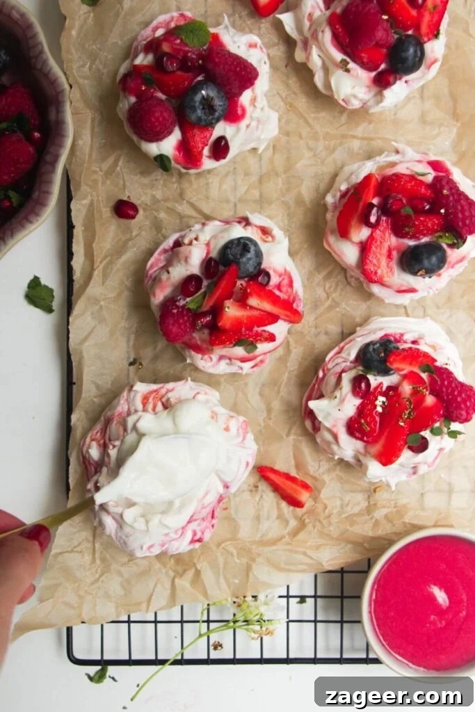 Heavenly Berry Ripple Cheesecake Pavlova Bites 17 Swirling raspberry puree through cheesecake mixture on top of a mini pavlova with more mini pavlovas in the background.