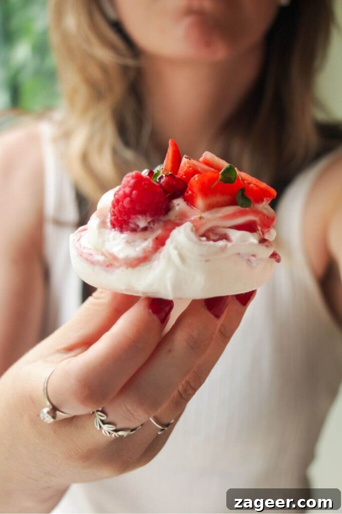 Heavenly Berry Ripple Cheesecake Pavlova Bites 21 Close up of someone holding up a mini pavlova topped with cheesecake yogurt and mixed berries.