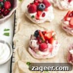 Two mini, berry topped pavlovas on a baking paper lined wire rack with more pavlovas behind them.