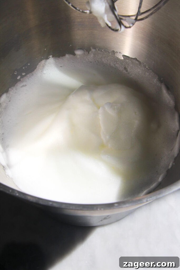 Heavenly Berry Ripple Cheesecake Pavlova Bites 5 Egg whites whipped to soft peaks in a large silver bowl.