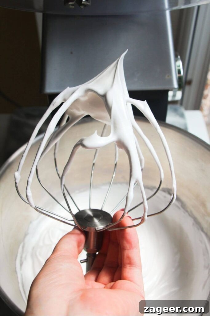 Heavenly Berry Ripple Cheesecake Pavlova Bites 6 Hand holding whisk attachment with stiff peaked meringue on the end.