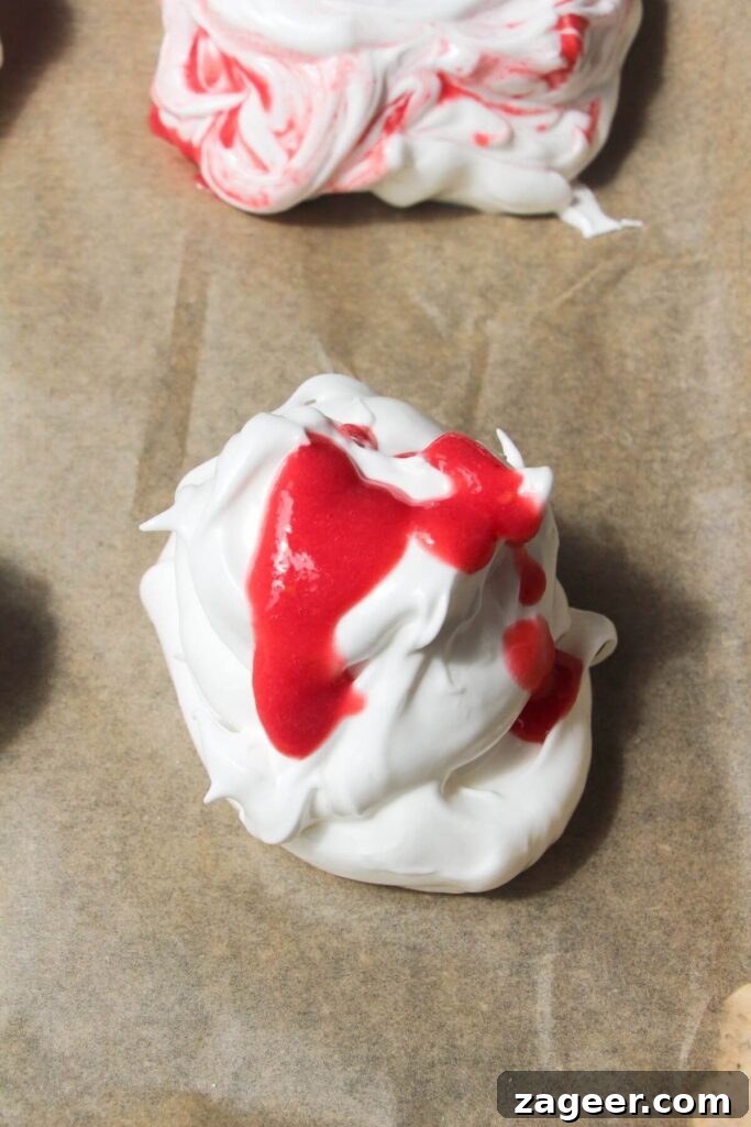 Heavenly Berry Ripple Cheesecake Pavlova Bites 9 Raspberry puree drizzled on top of meringue on a baking paper lined tray.