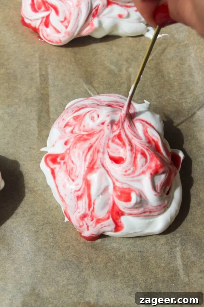 Heavenly Berry Ripple Cheesecake Pavlova Bites 10 Raspberry puree being swirled through meringue on baking paper lined tray with a skewer.