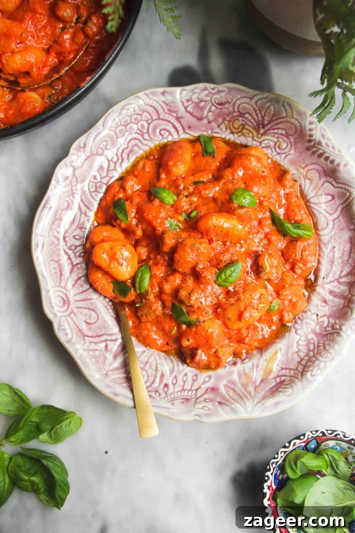 Creamy One-Pot Sausage Gnocchi Delight 2 A vibrant pink plate holds a generous serving of creamy tomato sausage gnocchi, garnished with fresh basil. A golden spoon is nestled beside it, inviting a taste of this comforting dish.