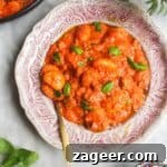 Creamy tomato sausage gnocchi on a pink plate with a gold spoon.