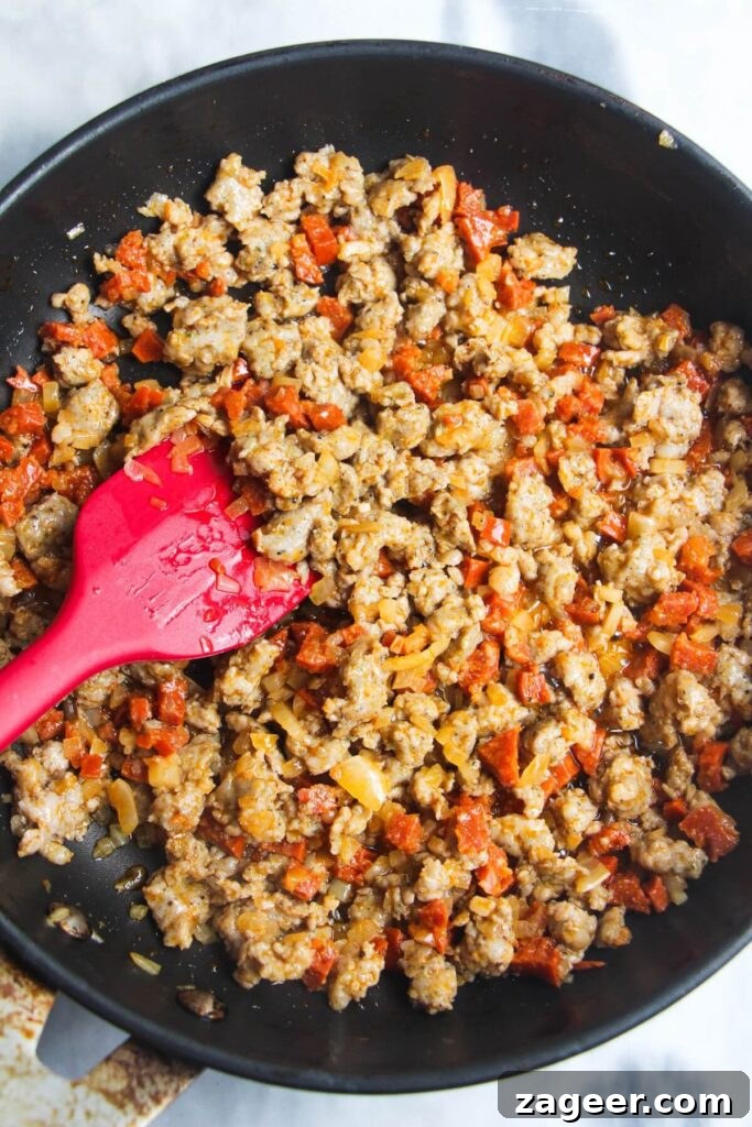 Creamy One-Pot Sausage Gnocchi Delight 5 The sausage meat, now fully cooked and lightly browned, is being stirred in the pan with a red spatula, ready for the next layer of flavors.